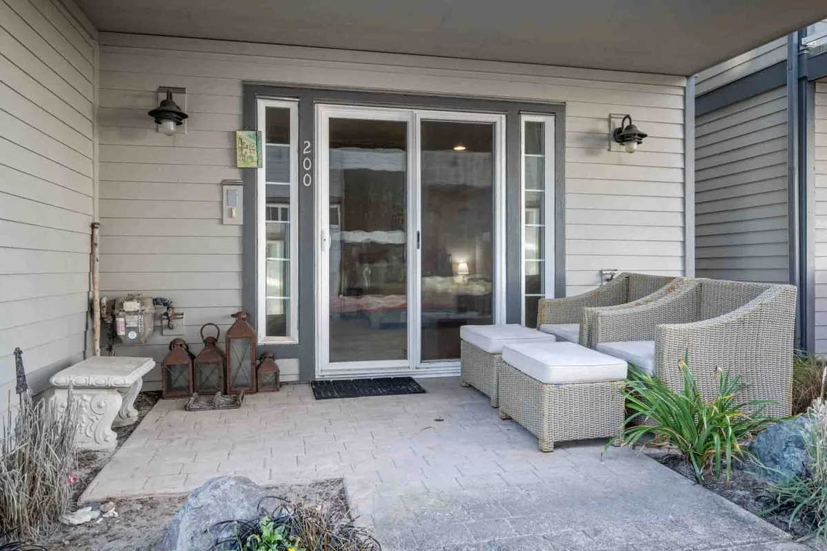A cozy and inviting exterior seating area just outside double glass doors. Wicker chairs and decorative lanterns are surrounded by lush plant life, providing a welcoming transition from home to the outdoors. The morning light filtering inside suggests a peaceful spot to relax after a day exploring downtown.