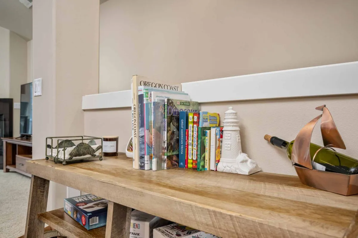 A charming bookshelf and wooden shelf display a collection of books, a decorative lighthouse, wine bottle, ship sculpture, and a glass terrarium. This setting suggests quiet afternoons of reading or intimate gatherings with wine.