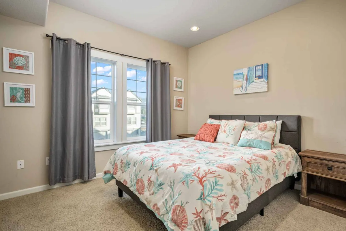 The photo shows a cozy bedroom with a bed adorned in coral-patterned bedding, set beside a large window streaming with natural light. Decorative wall art and soft furnishings enhance the inviting, serene atmosphere. The scene suggests a peaceful spot for morning coffee or relaxing after a day of exploration.