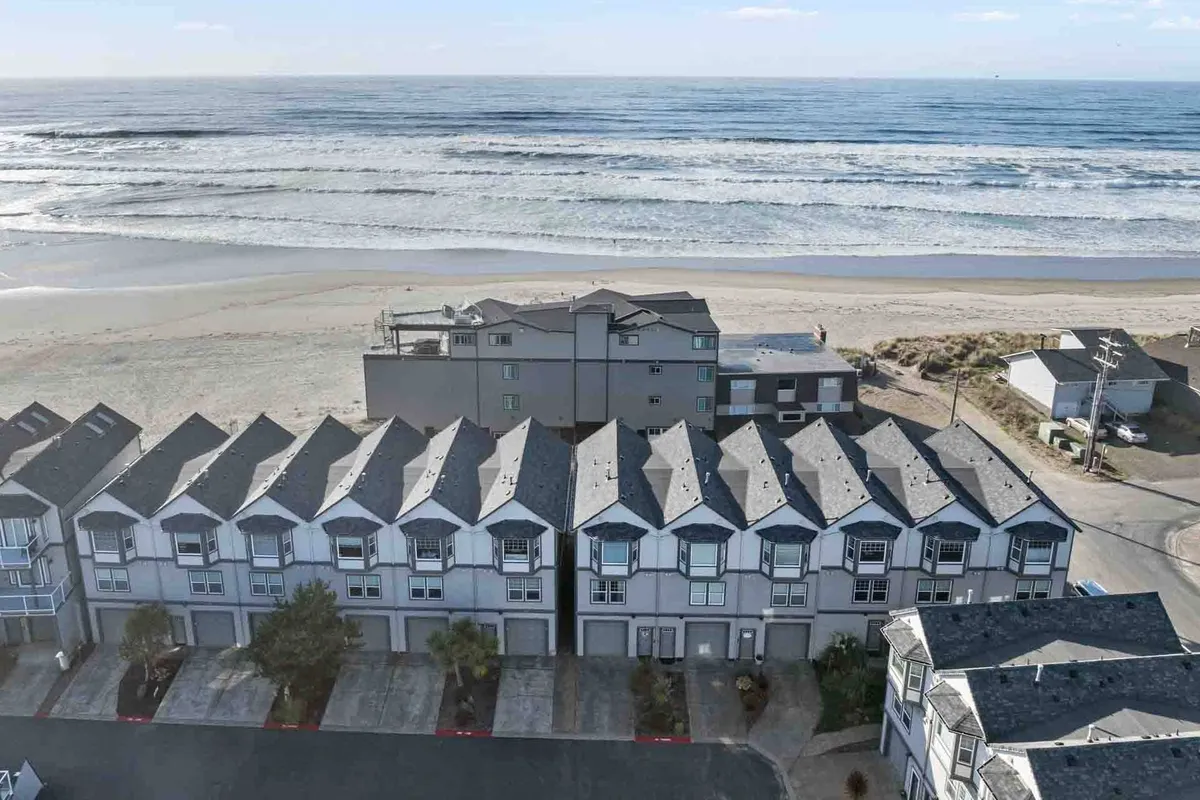 This image showcases a row of charming beach houses directly facing the expansive sandy shoreline, with gentle ocean waves rolling in. The composition highlights both the proximity of the homes to the beach and the inviting nature of the area for activities such as beachcombing, sunbathing, or early morning walks.
