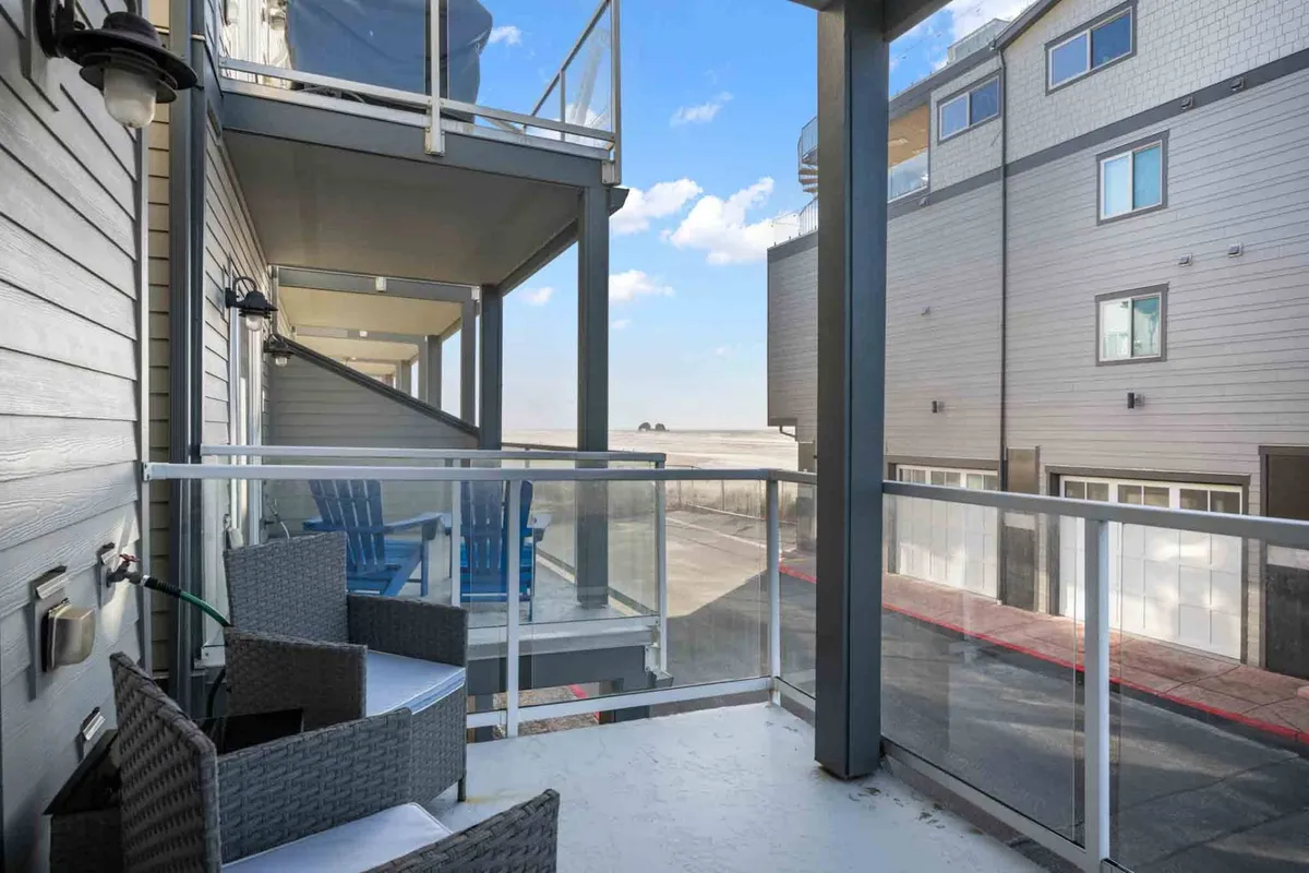 An exterior shot of a balcony with blue chairs and glass railings, offering open views and a clear connection to outdoor relaxation. The setting suggests a prime spot for sunset watching or morning coffee, tying directly to the ocean-view deck described in the text.