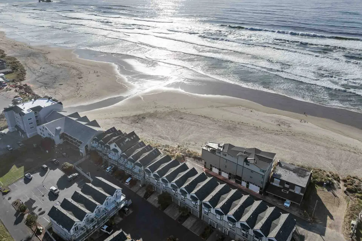 A panoramic view of the beach, ocean waves, coastal buildings, and convenient parking area. The lively beach scene is perfect for families playing, sunbathers, surfers, and shell collectors, encapsulating a day filled with seaside fun and relaxation.
