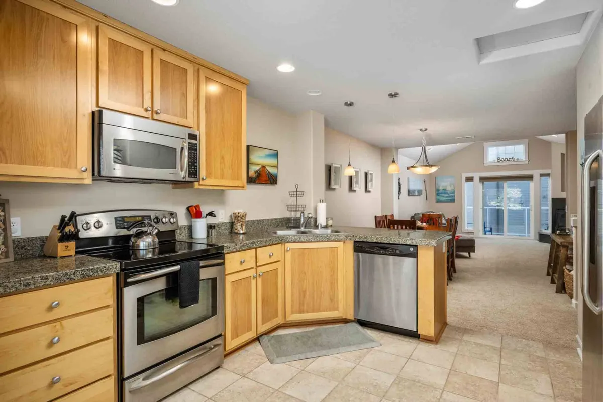 A tastefully decorated kitchen with a central island, gleaming stainless steel appliances, and an adjacent dining area. Artwork adorns the walls, and the room radiates with a friendly, welcoming energy, ideal for cooking, entertaining, or sharing morning coffee.