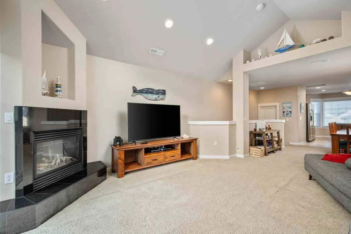 A warm, inviting living space with a fireplace, TV, wooden furniture, and nautical decor such as a decorative fish and a model sailboat. The room suggests cozy family gatherings, movie nights, and evenings by the fire.