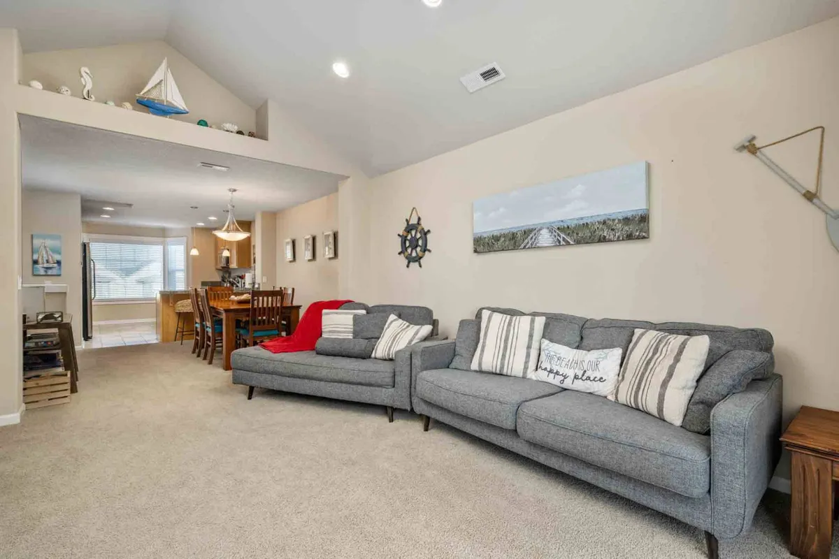 An open living and dining area with plush sofas, a family-sized dining table, and coastal decorative accents. Subtle lighting fixtures add warmth, creating a welcoming space for socializing, unwinding, and hosting gatherings.