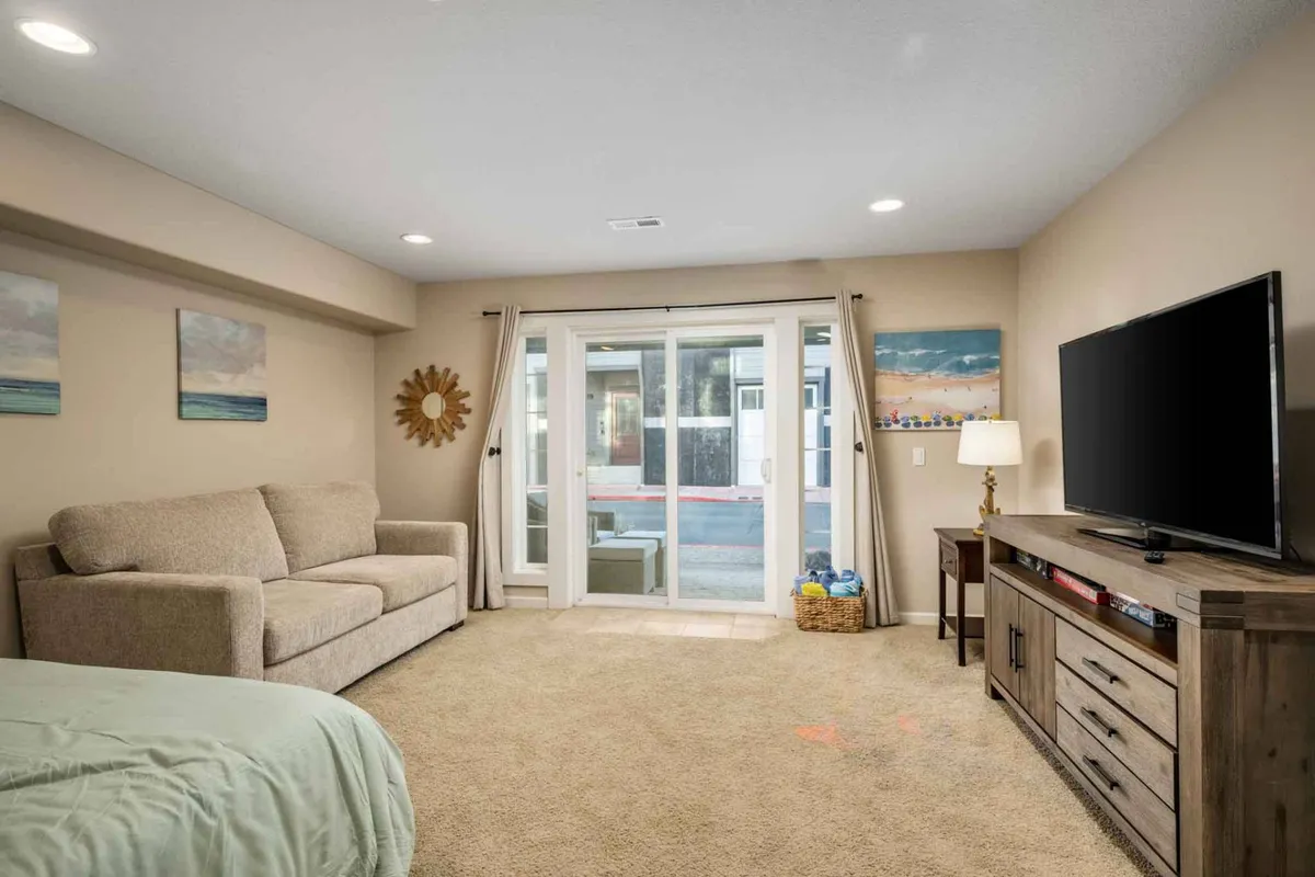 A welcoming interior scene showcasing a comfortable sofa, a TV, sliding glass doors that connect to the outdoors, a decorative mirror, and artwork. The space is designed for relaxing, watching movies, or sharing casual conversations.