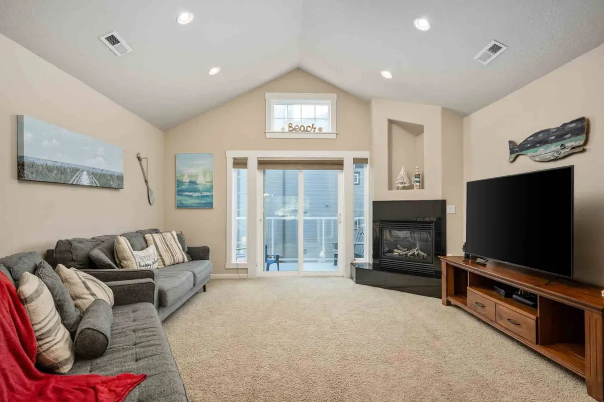 This image features a comfortable rumpus room setup with a plush sofa adorned with pillows, a fireplace, a large TV, and glass doors leading to the outside. The atmosphere is warm and inviting, ideal for relaxing, entertaining, or cozy movie nights.